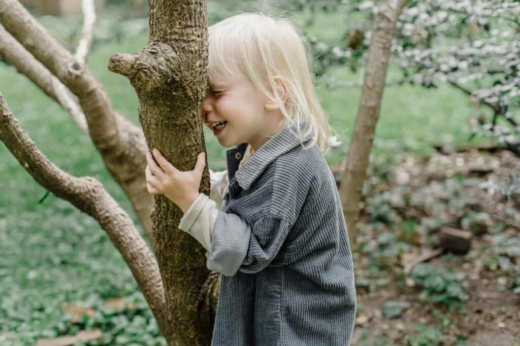 A happy young boy is standing in front of the tree trunk