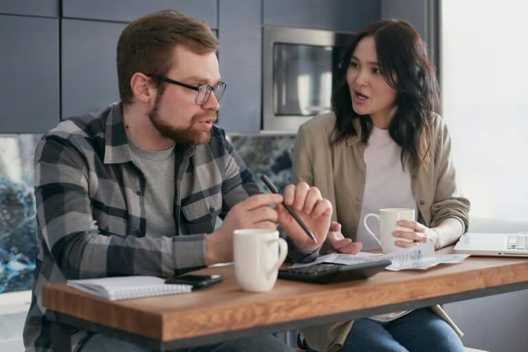 A couple with pen, papers, laptop, calculator, and mugs of coffee on the table budgeting for the house move in the concept of 'Hendon's removals cost'.